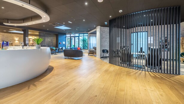 Un hall d’entrée spacieux, doté d’un comptoir d’accueil incurvé, d’un espace salon et offrant une vue sur l’extérieur.