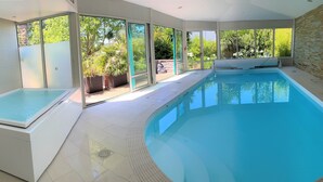 Une piscine intérieure moderne avec des parois en verre transparent, un sol carrelé et une vue sur la verdure environnante.