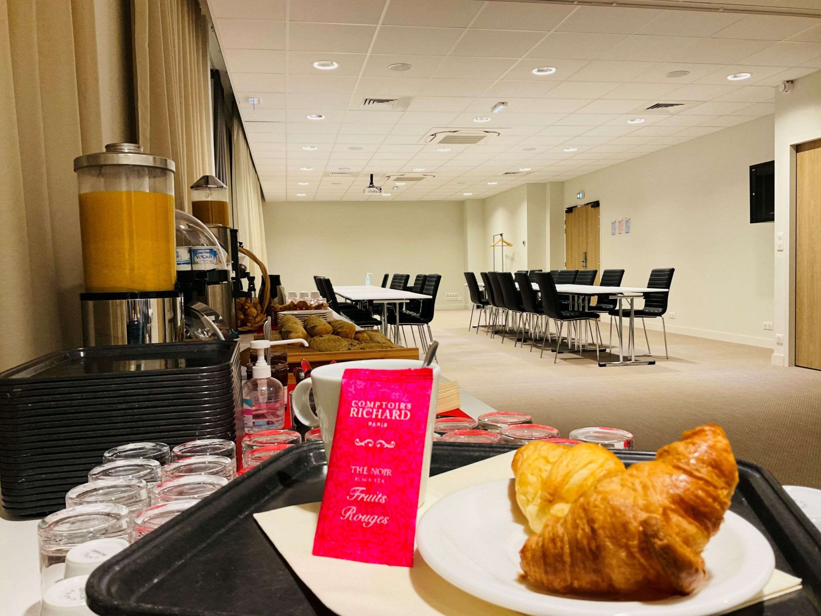 A breakfast setup with a croissant on a tray, a coffee machine, and a sign for Richard Blanc tea.