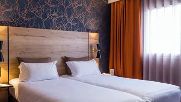 Habitación de hotel con cama doble, cabecera de madera, mesita de noche, lámpara y ventana con cortinas.