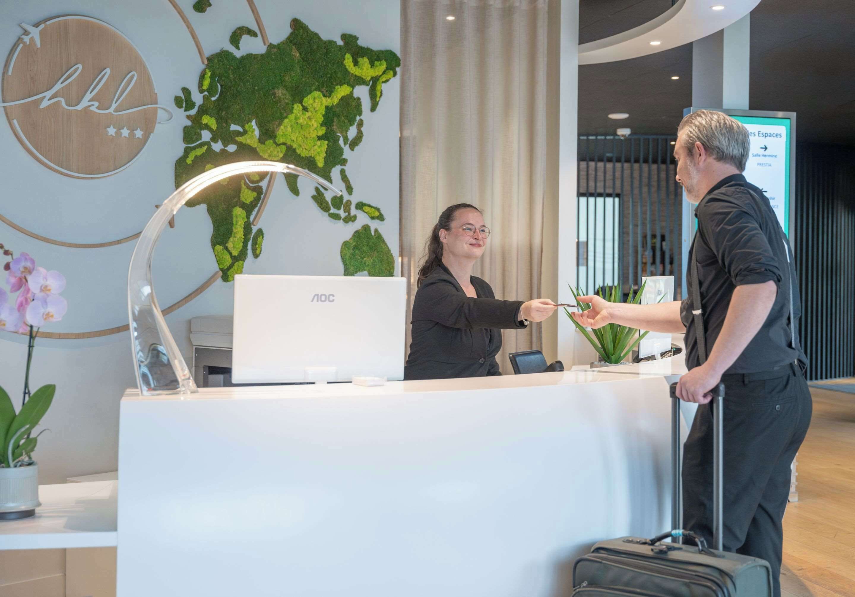 Un mostrador de recepción con una computadora portátil, un mapa mundial y un cartel que indica las habitaciones del hotel.