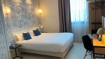 Une chambre d’hôtel moderne avec un lit bien fait, un bureau avec une chaise et une grande fenêtre avec des rideaux.