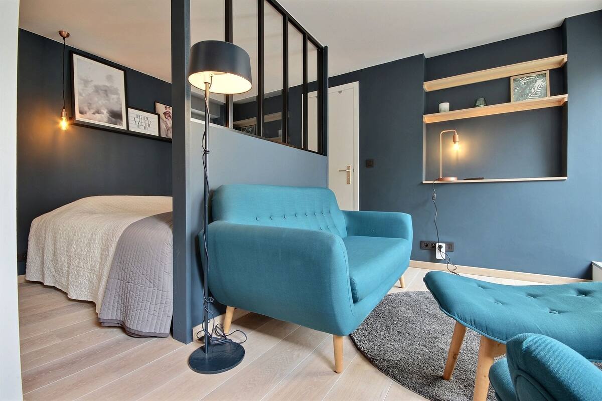 Een moderne slaapkamer met een bed, een blauwe fauteuil, een kleine tafel en een vloerlamp.