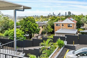 A residential area with a view of a city skyline, a house with a red roof, and a fenced yard with palm trees.