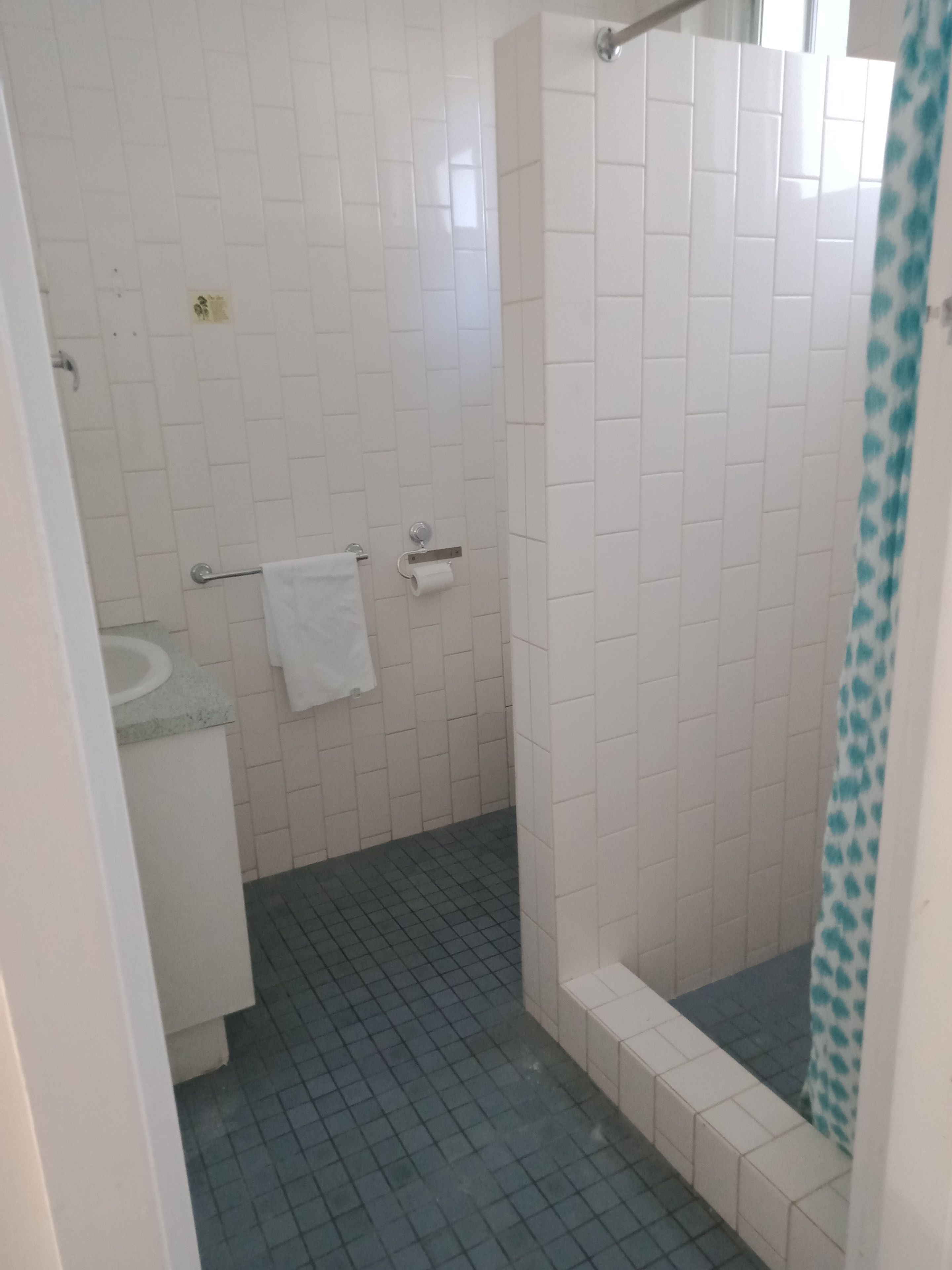 A bathroom with white tiles, a shower with a blue curtain, and a white towel hanging on a rack.