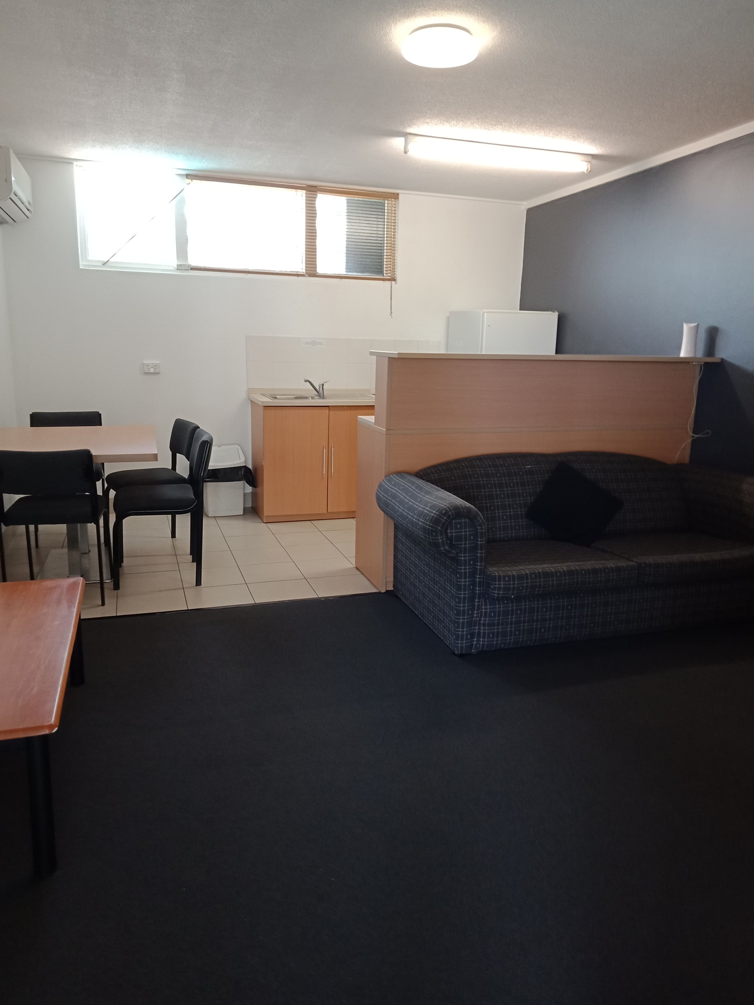 Un espacio habitable compacto con kitchenette, zona de comedor con mesa y sillas, y un sofá.