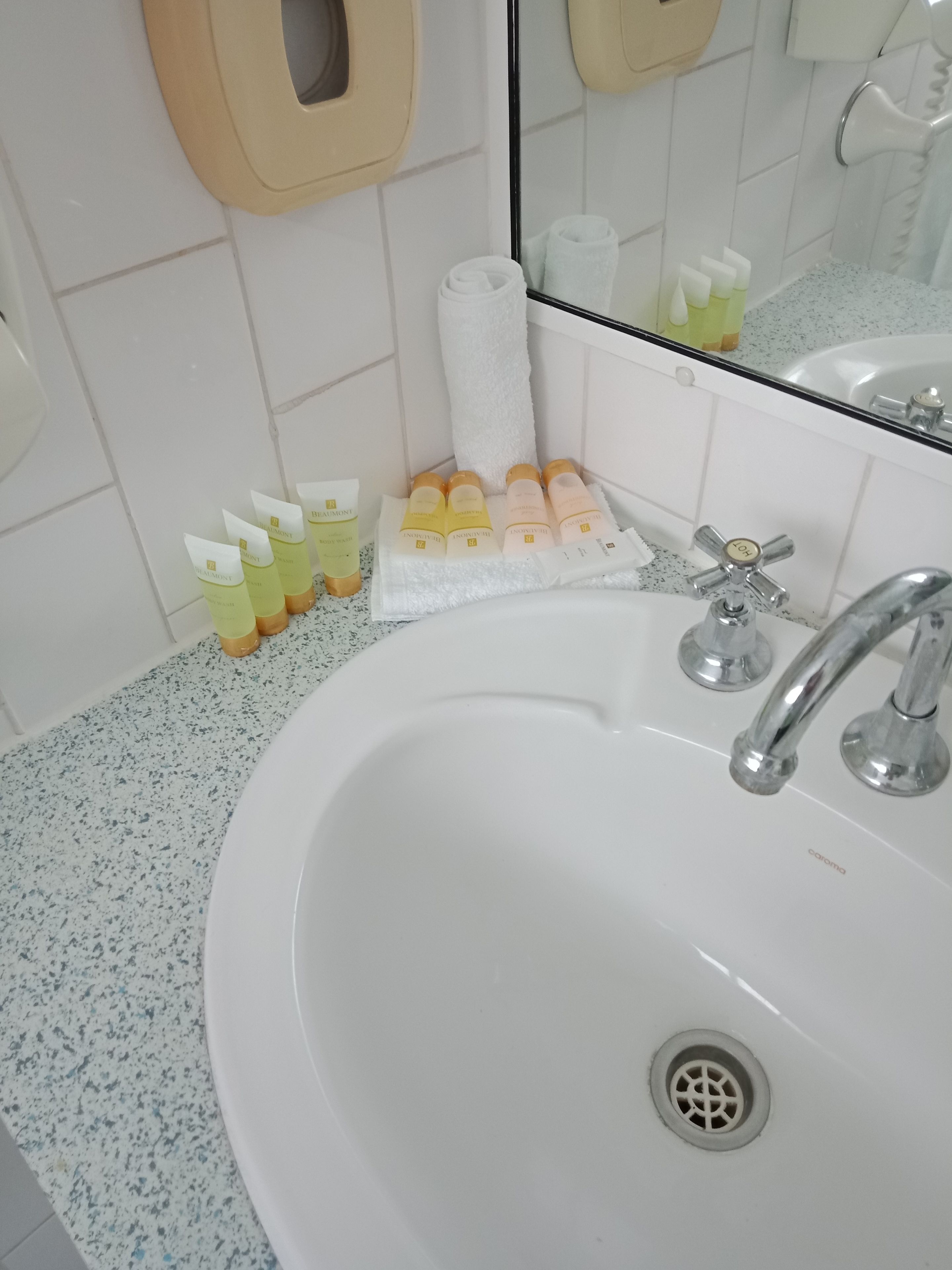 A bathroom with a white sink, a mirror, and toiletries including bottles and a towel.