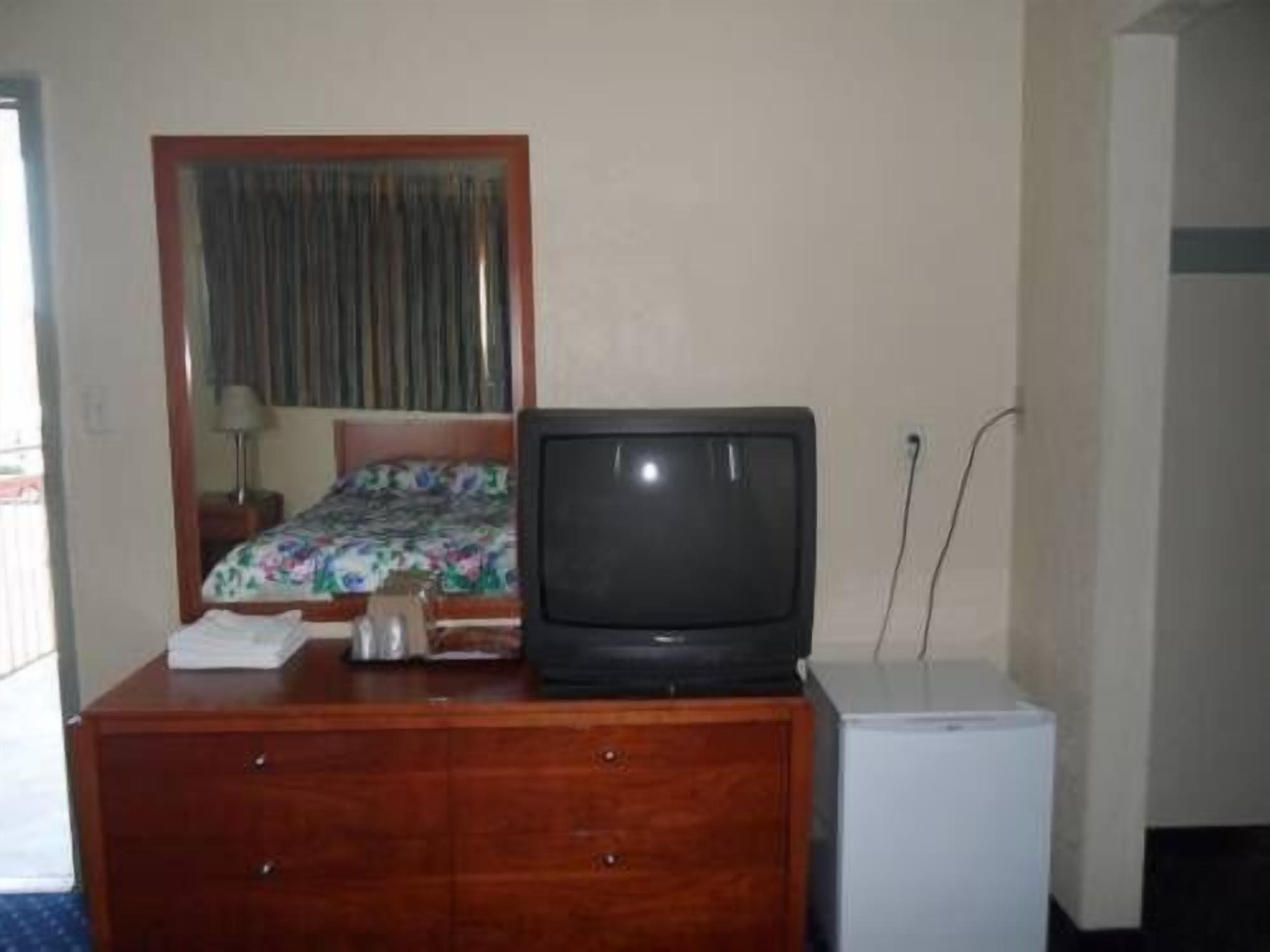 A hotel room with a bed, a television on a wooden dresser, and a small white appliance.