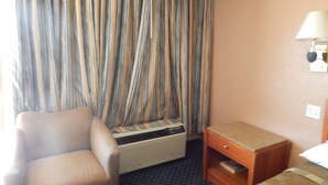 A hotel room with a striped curtain, a chair, a small table, and a bed. - Bay Bridge Inn (Oakland)