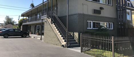 A two-story building with a balcony, a staircase, and a gated driveway.