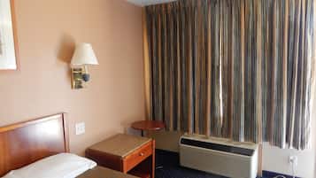 Una habitación de hotel con una cama, una mesita de noche, una lámpara, un ventanal con cortinas y un equipo de aire acondicionado.