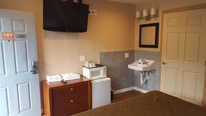 A hotel room with a bed, a small desk with a microwave, a sink, and a TV mounted on the wall. - Bay Bridge Inn (Oakland)