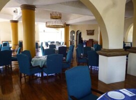 Uma sala de jantar ampla com cadeiras e mesas azuis, piso de madeira e um candelabro.