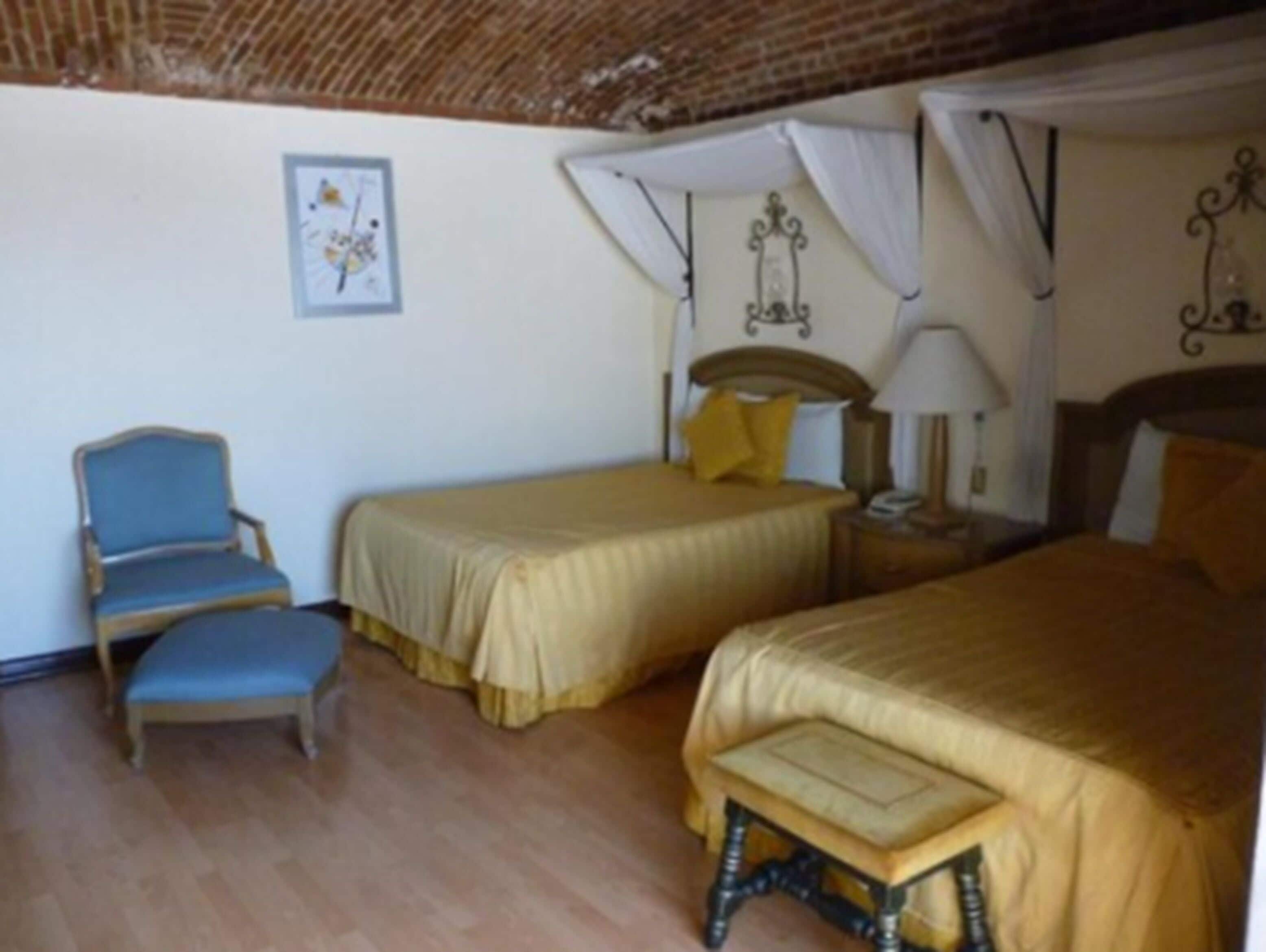 A room with two beds, a chair, a bedside table with a lamp, and a picture on the wall.