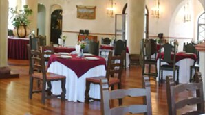 A dining area with wooden chairs and tables, a chandelier, and a large vase with flowers.
