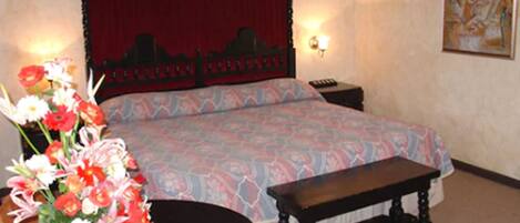 A hotel room with a bed, a bedside table, a chair, and a small round table with a vase of flowers.