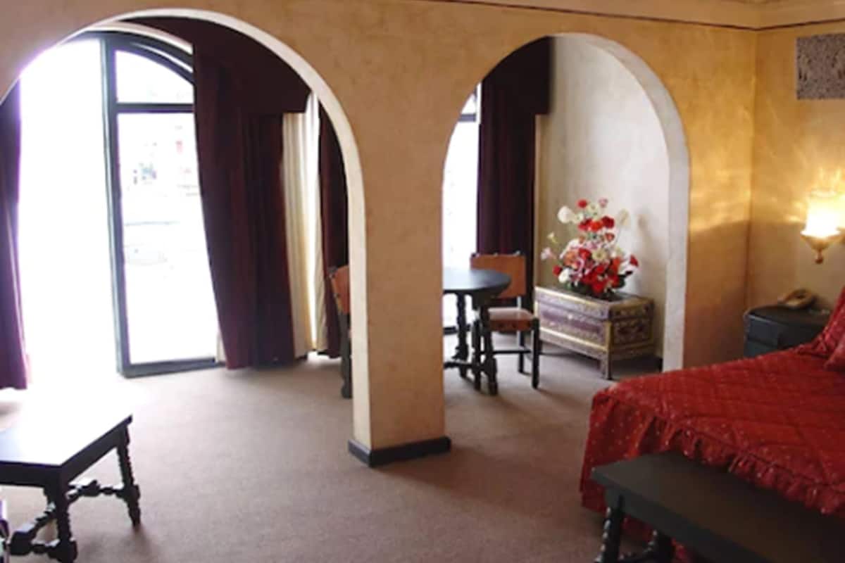 Habitación de hotel con cama, escritorio, silla y una pequeña mesa. Se observan dos arcos que dan a otra habitación.