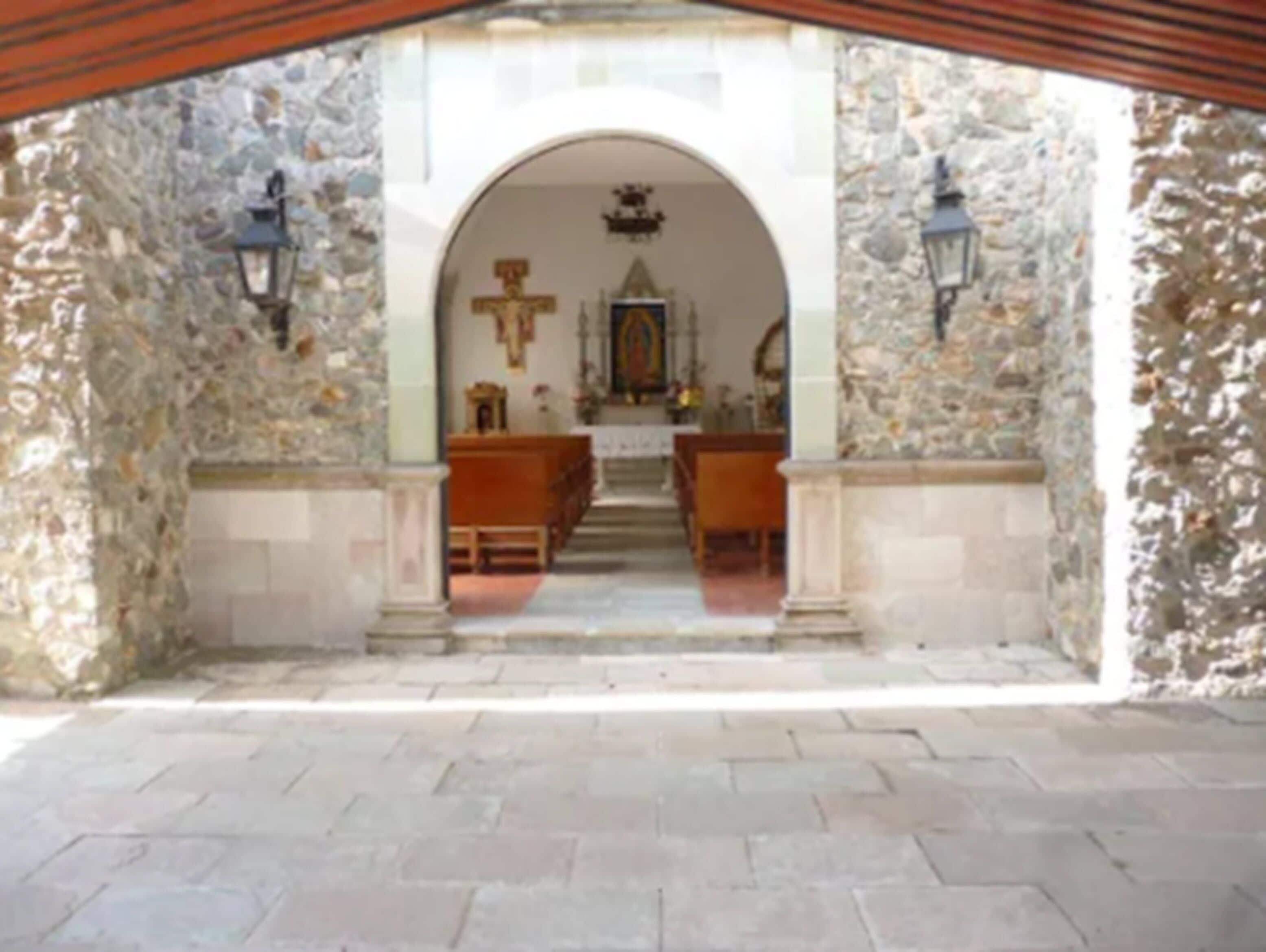 An arched entrance to a church with stone walls and wooden pews inside.