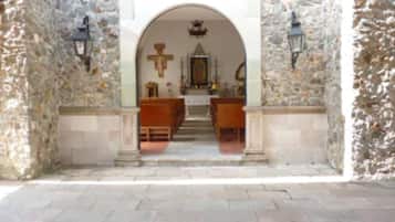 An arched entrance to a church with stone walls and wooden pews inside.
