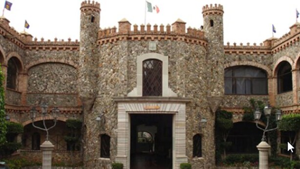 A stone building with a central entrance, arched windows, and flags.