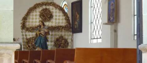 A church interior with wooden pews, a statue, and religious paintings.