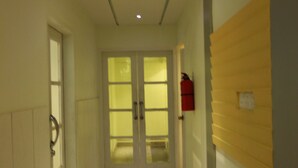 A narrow hallway with a door at the end, a fire extinguisher on the wall, and a light fixture on the ceiling. - Hotel Ornate (Dhaka)