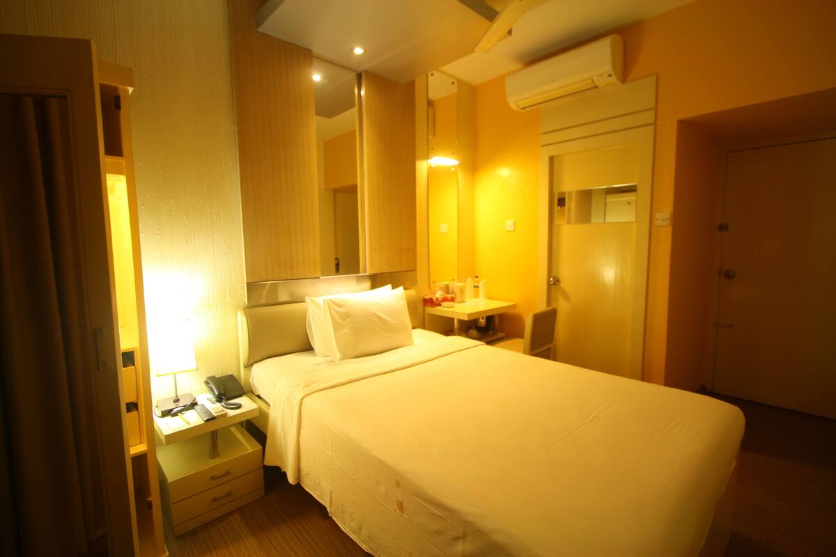 A hotel room with a bed, bedside table, lamp, and a mirror.