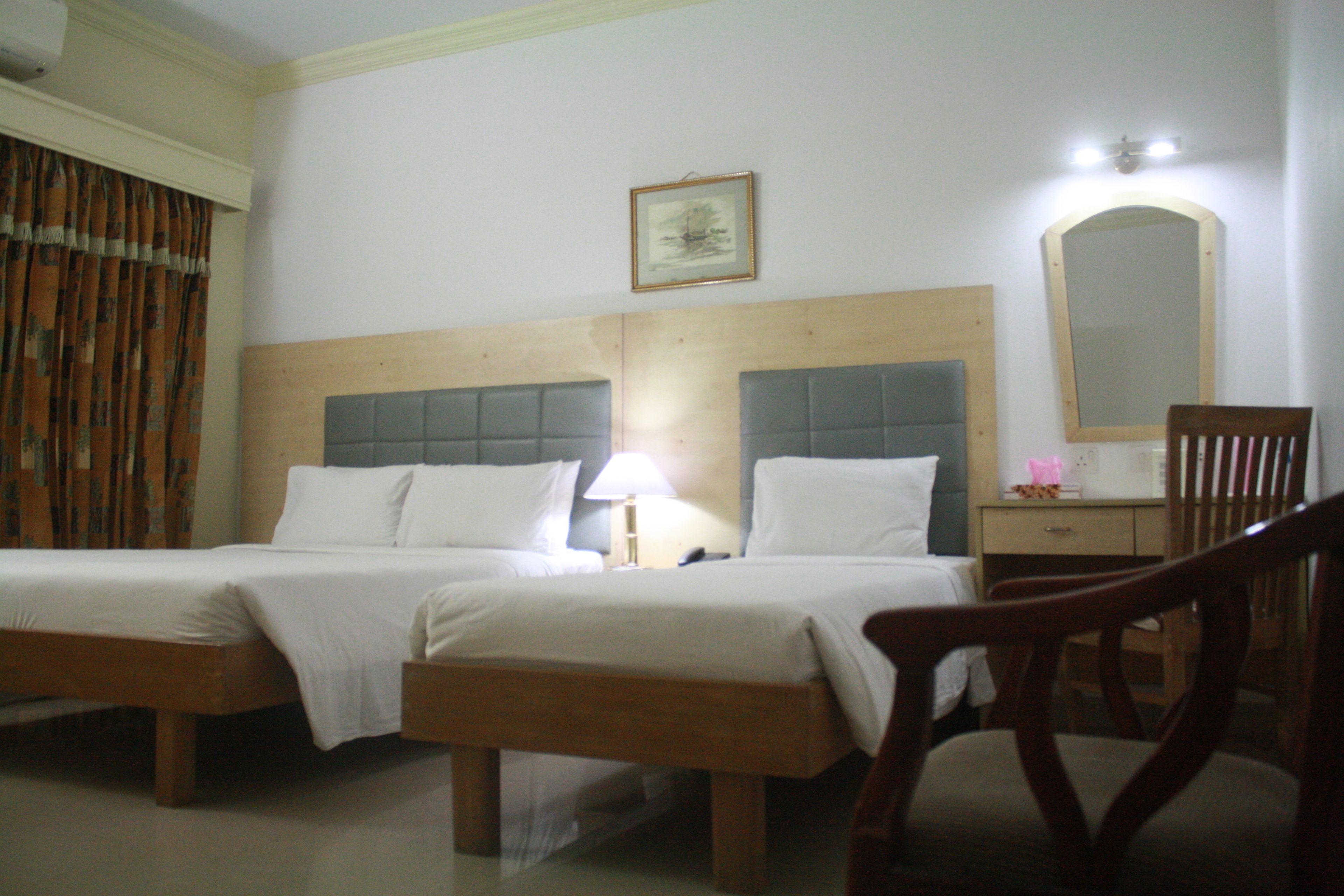 Una habitación de hotel con dos camas, una mesita de noche con lámpara, un espejo y una silla.
