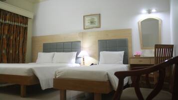 Una habitación de hotel con dos camas, una mesita de noche con lámpara, un espejo y una silla.