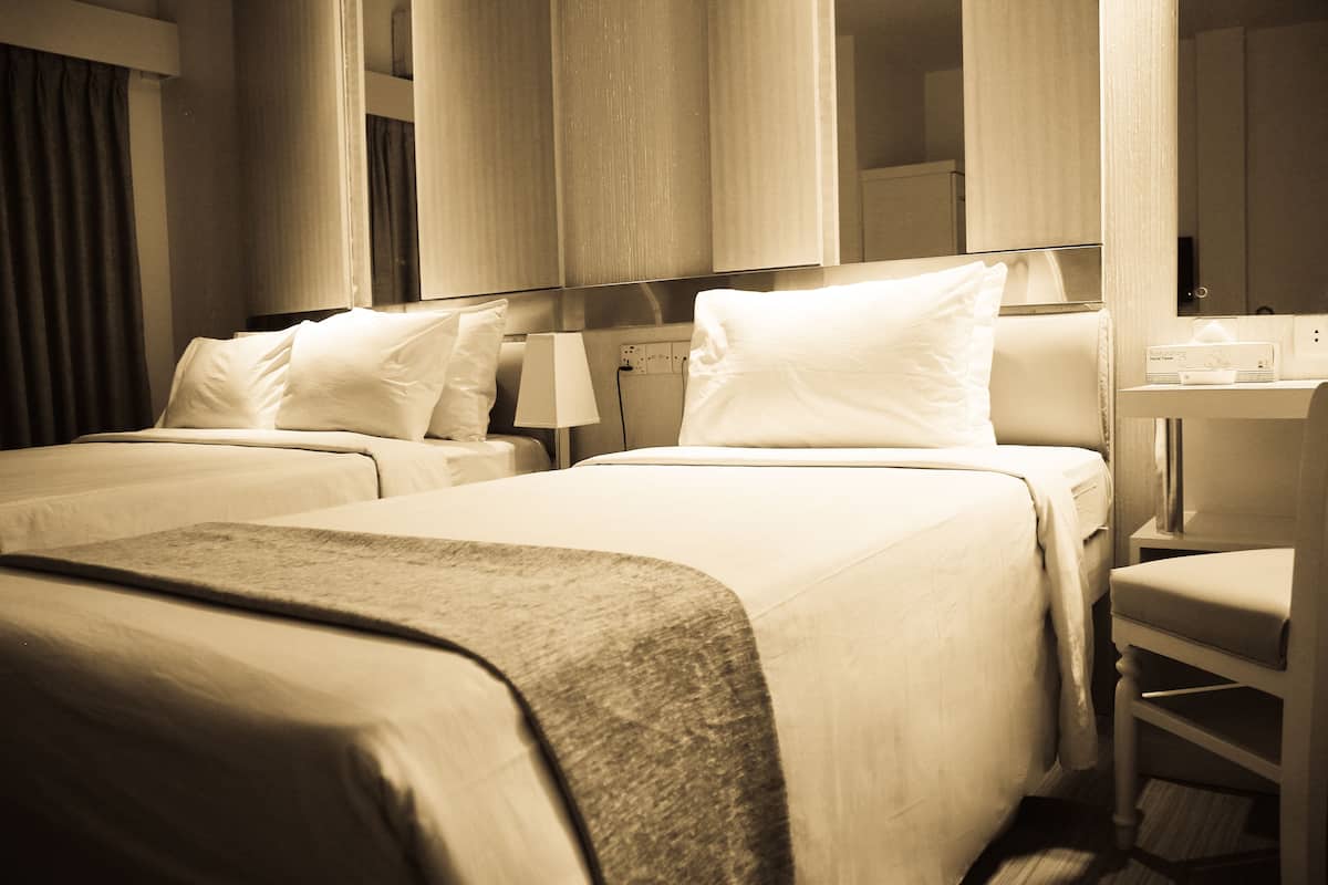 A hotel room with two beds, a bedside table, a lamp, and a mirror.