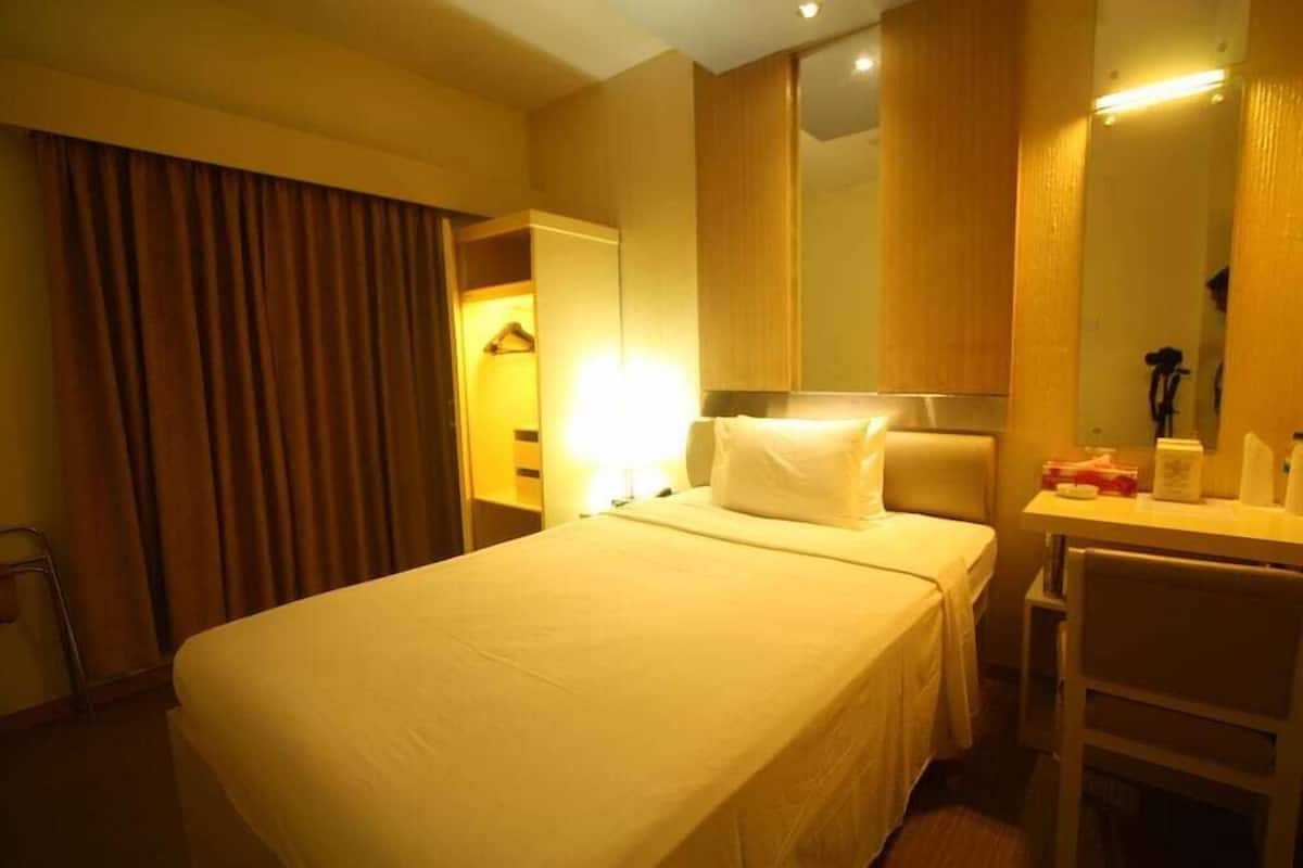A hotel room with a bed, a desk, a chair, a mirror, and a wardrobe.