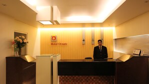 A hotel reception desk with a man standing behind it, a framed floral arrangement, and a sign that reads "Hotel Ornate". - Hotel Ornate (Dhaka)