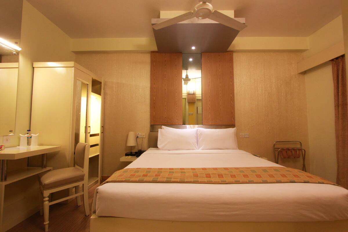 A hotel room with a bed, a desk, a chair, a mirror, and a wardrobe.