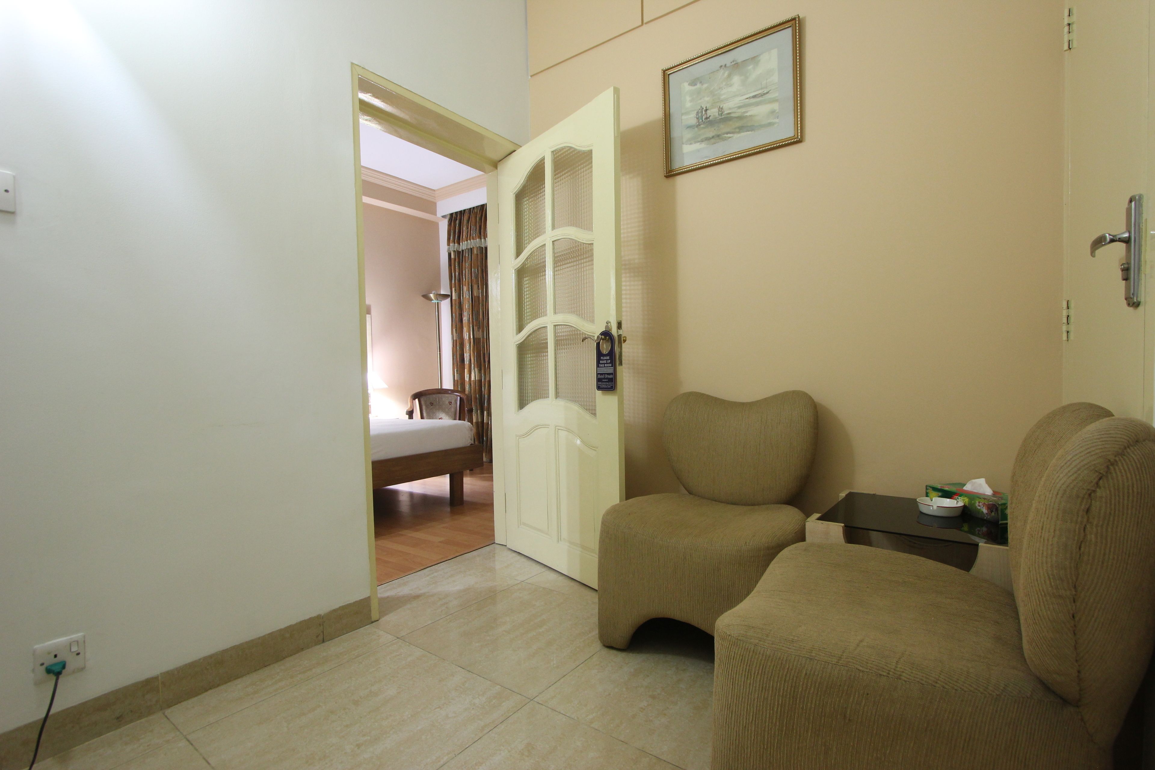 Une pièce avec un canapé beige, une petite table sur laquelle se trouve une boîte de mouchoirs, une porte donnant sur une autre pièce et un tableau accroché au mur.