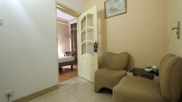 Une pièce avec un canapé beige, une petite table sur laquelle se trouve une boîte de mouchoirs, une porte donnant sur une autre pièce et un tableau accroché au mur.
