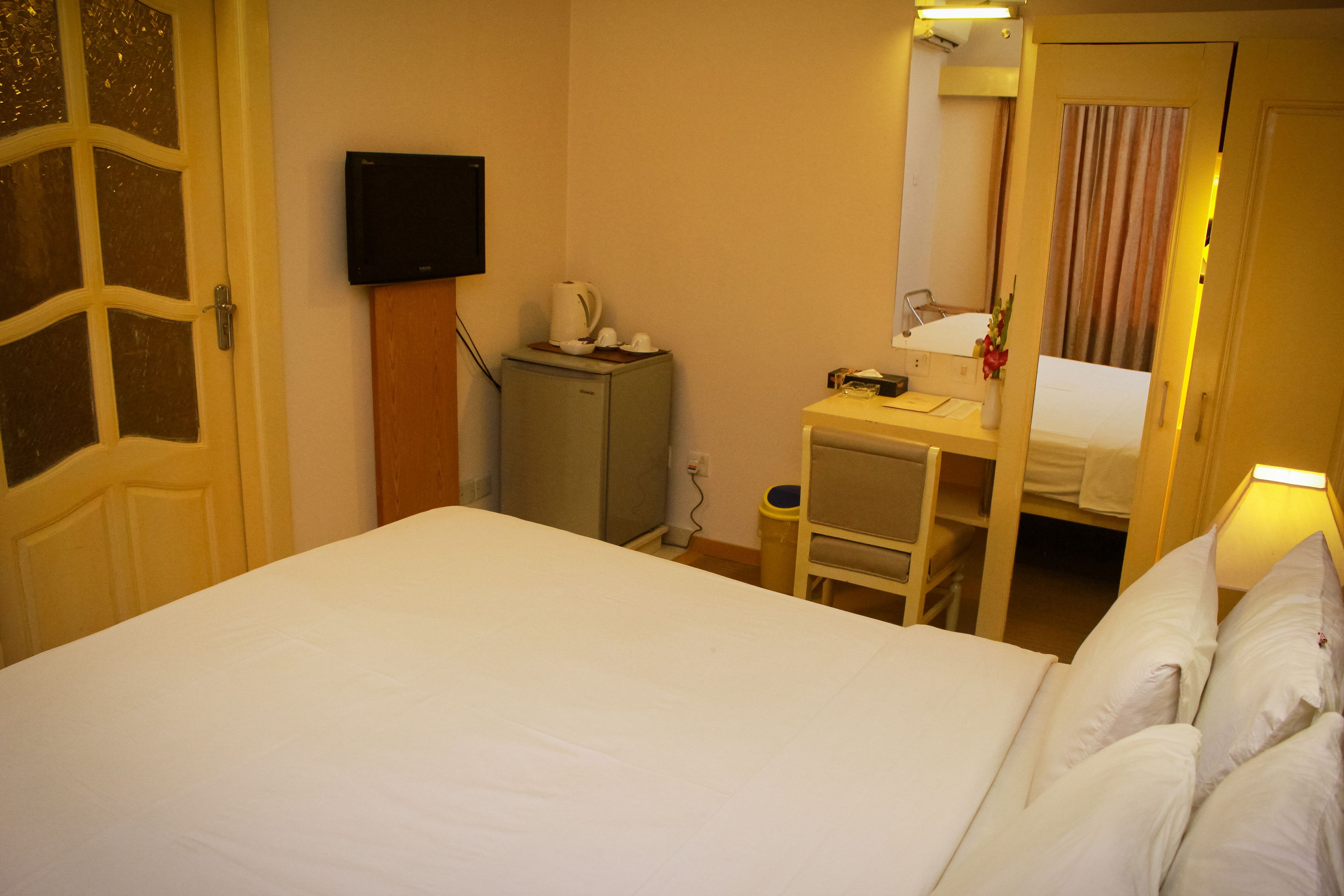 A hotel room with a bed, a desk with a chair, a small cabinet, a television, and a bathroom visible through an open door.