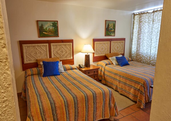 A hotel room with two beds, each with striped bedding and matching headboards. There is a nightstand with a lamp between the beds, and two paintings on the wall above each bed.