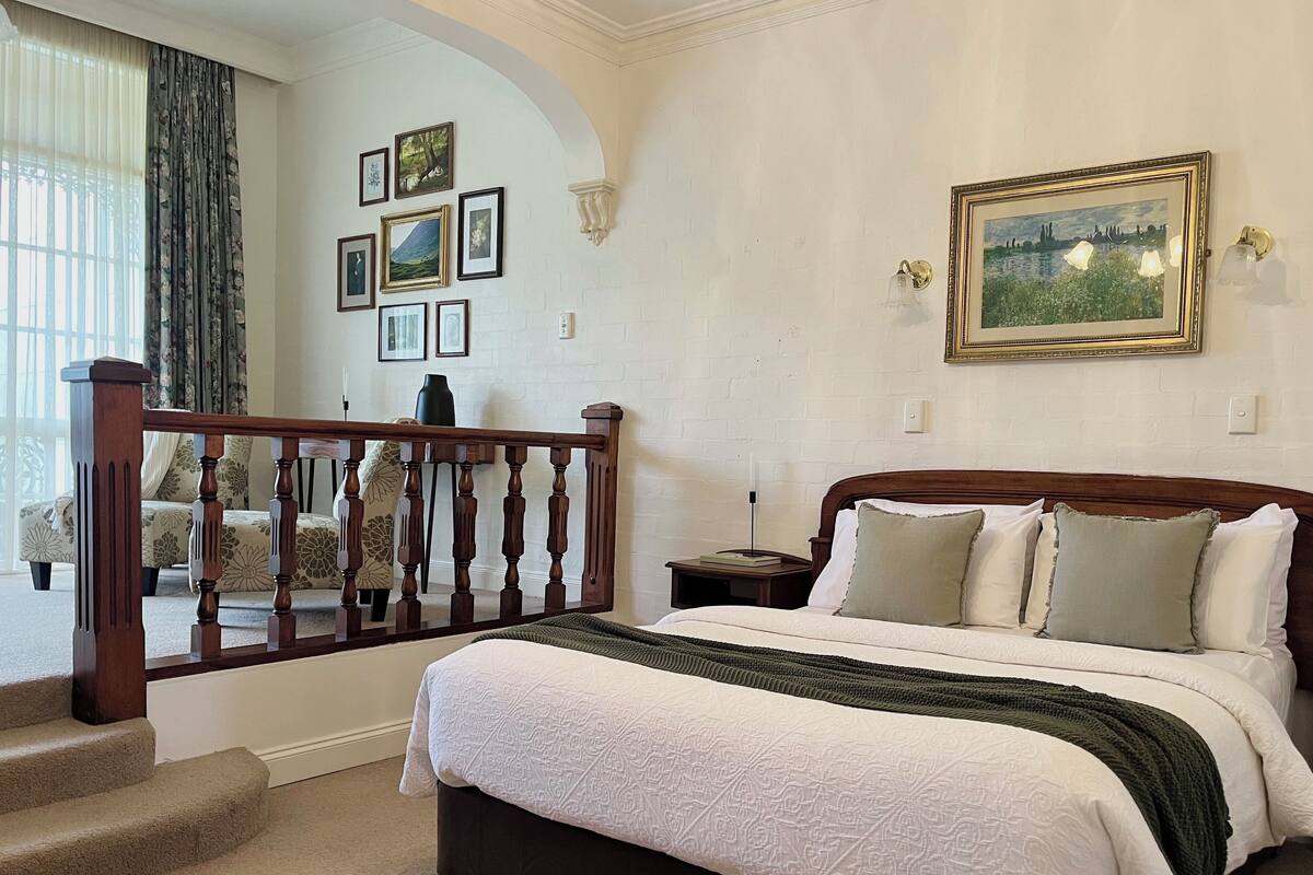 A bedroom with a large bed, a wooden staircase, and a wall decorated with framed pictures.