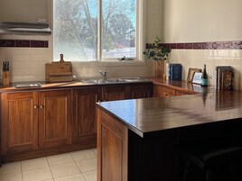 Cozinha com armários de madeira, pia de aço inoxidável e janela com vista para árvores.