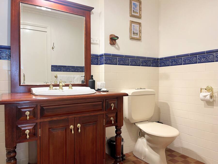 Een badkamer met een houten wastafelmeubel, een witte wasbak, een spiegel, een toilet en blauwe betegelde wanden.