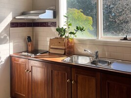 Cozinha com armários de madeira, pia de aço inoxidável e janela com vista para árvores.