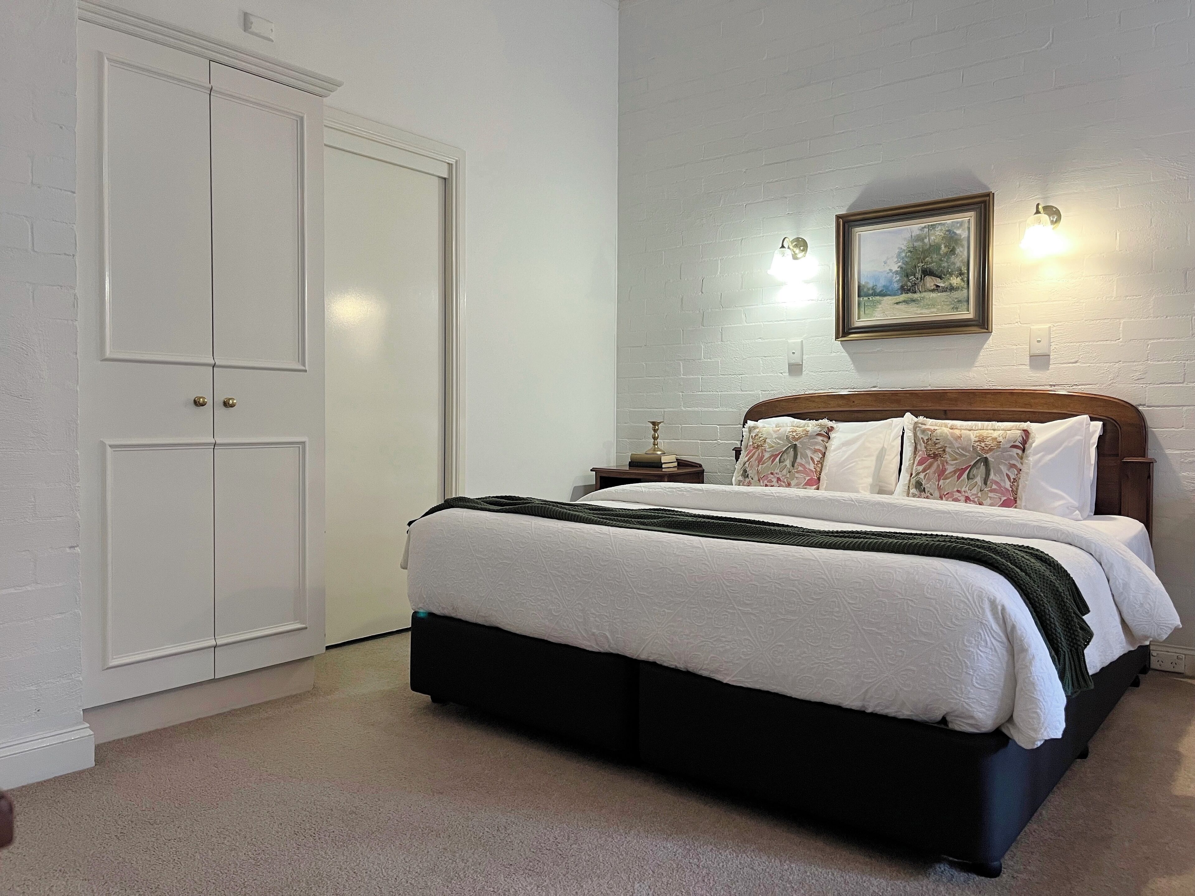 Een slaapkamer met een bed, een nachtkastje, een ingelijst beeld aan de muur en een witte deur.