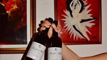 Two bottles of wine with labels, a framed painting, and a poster on a wall.