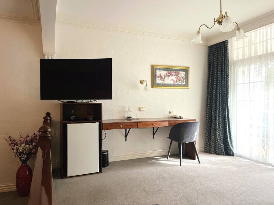 Una habitación con escritorio, silla, televisor y un refrigerador pequeño.