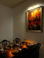 Uma sala de jantar com uma mesa posta para dois, um quadro emoldurado acima da mesa e uma parede de tijolos.