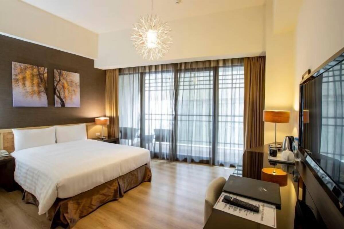 A hotel room with a large bed, a desk with a computer, a TV, and a piano.