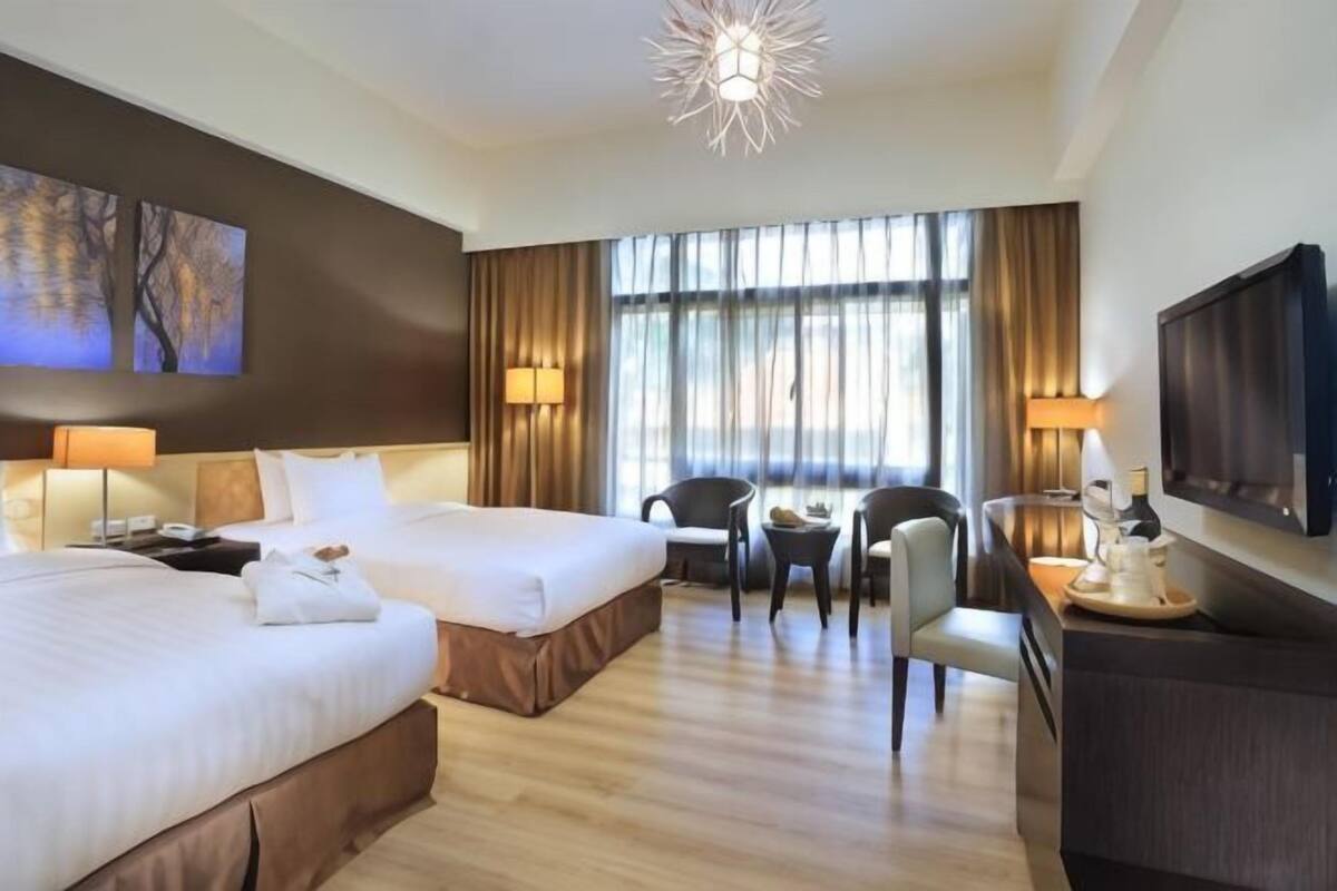 A hotel room with two beds, a desk, chairs, a TV, and a large window with curtains.