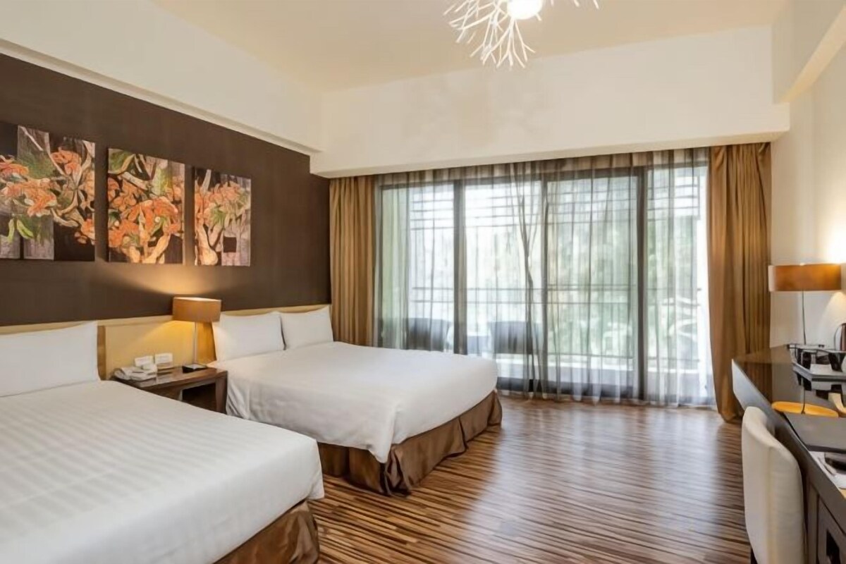 Hotellihuone, jossa on kaksi sänkyä, työpöytä ja suuri ikkuna, jossa on verhot.