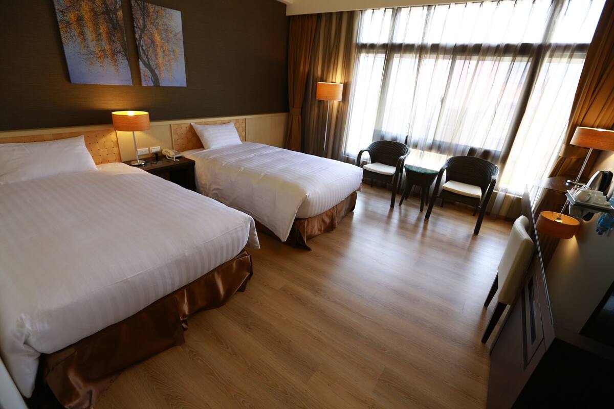 A hotel room with two beds, a desk, a chair, and a window with curtains.