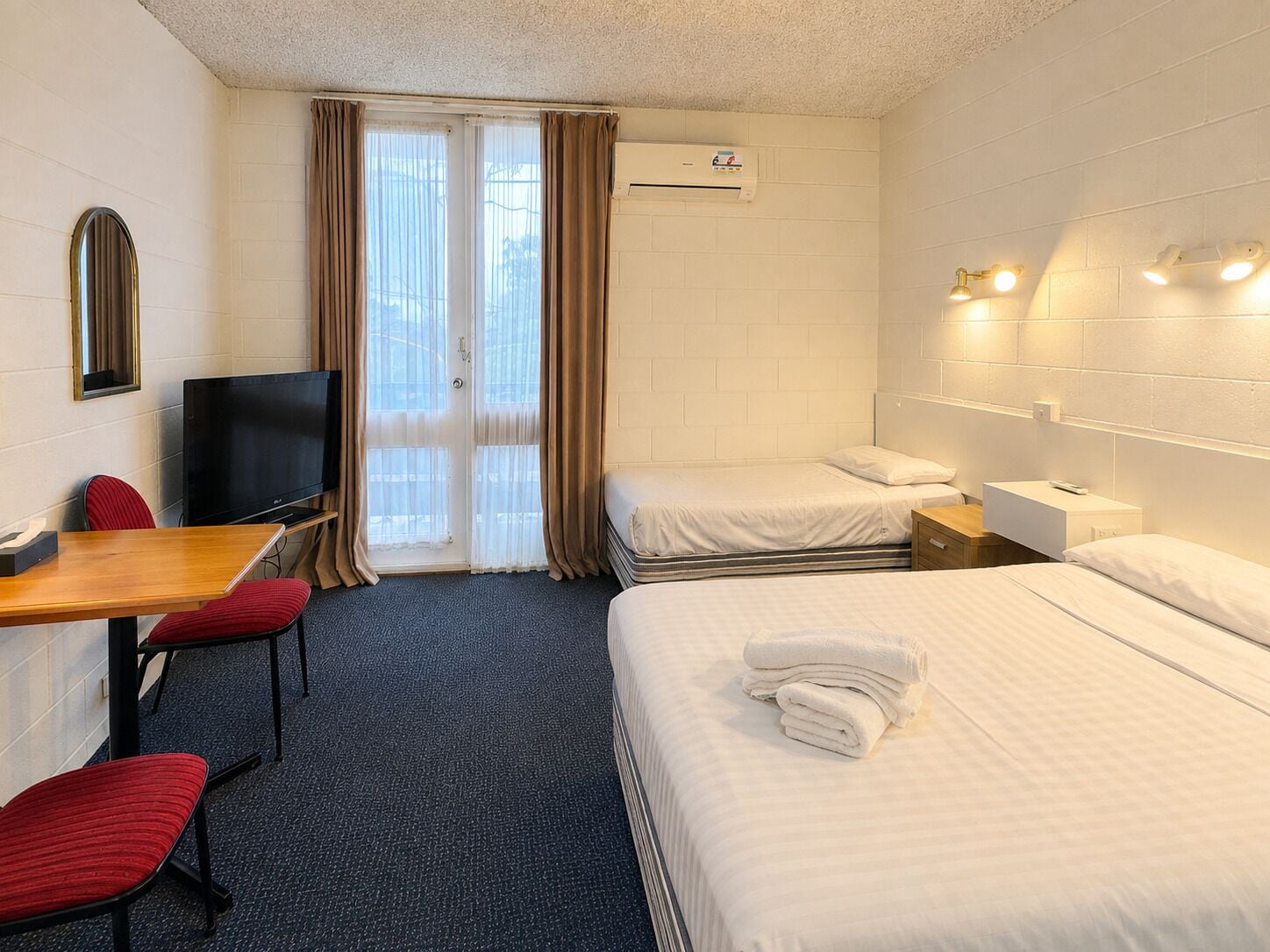 A hotel room with a bed, a desk with a chair, a television, and a window with curtains.
